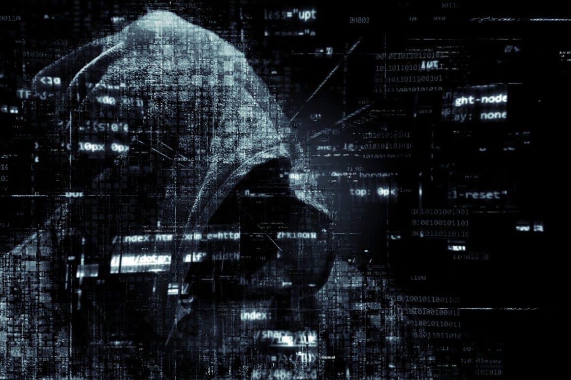 Un hacker à capuche devant un fond noir avec des incrustations de sigles numériques