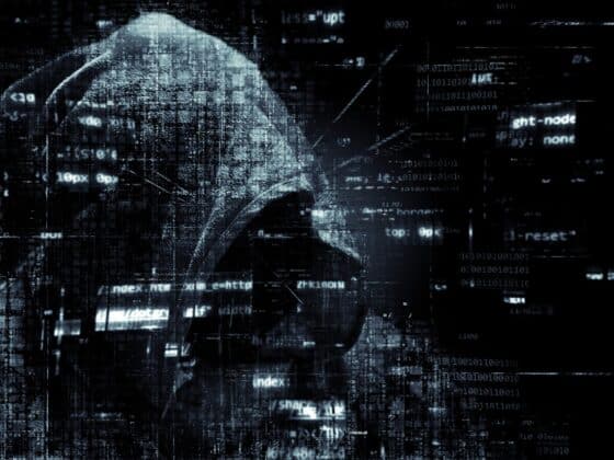 Un hacker à capuche devant un fond noir avec des incrustations de sigles numériques