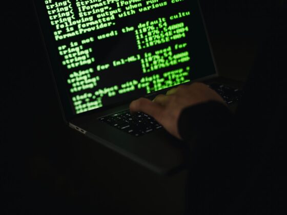 crop hacker typing on laptop with information on screen