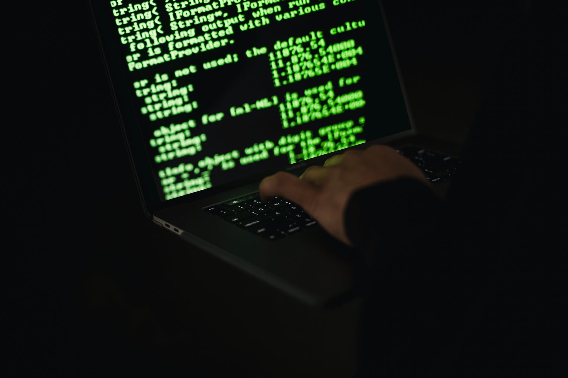 crop hacker typing on laptop with information on screen
