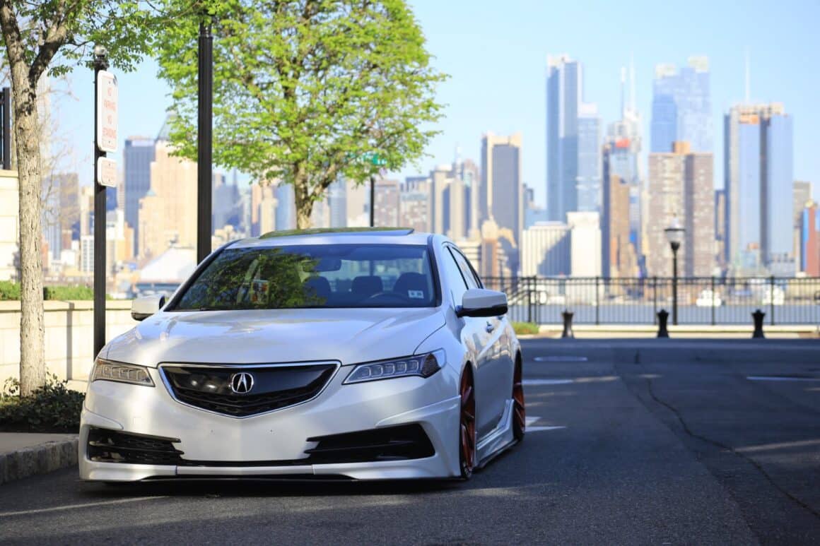 white acura sedan on gray asphalt road near green tree at daytime