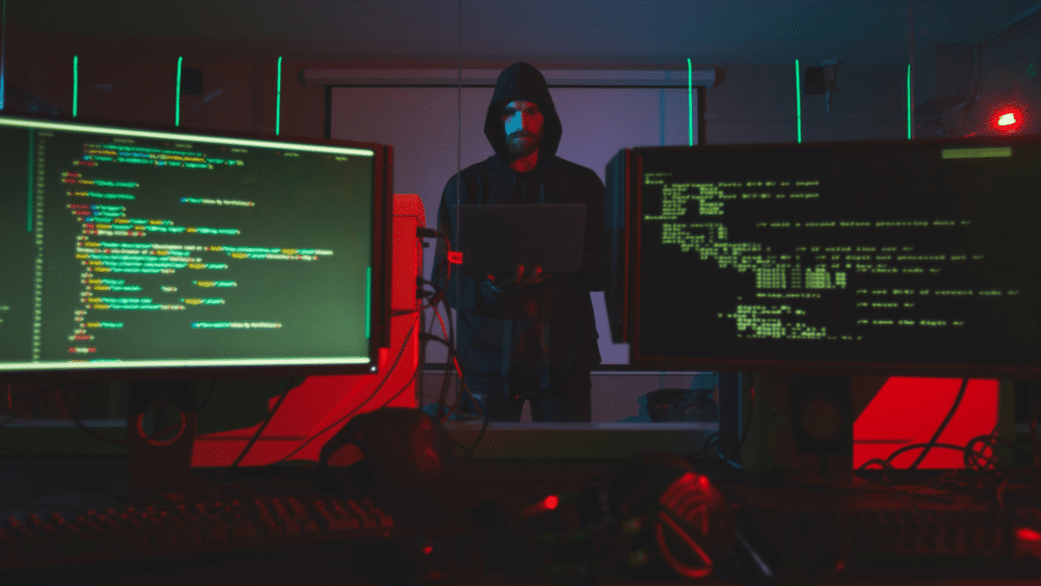 Un pirate à capuche devant des écran avec du code