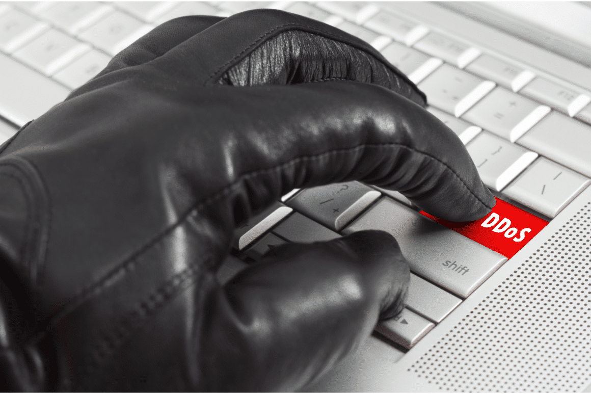 Un clavier avec une touche DDOS et un gant noir qui s'apprête à appuyer dessus