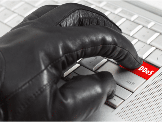 Un clavier avec une touche DDOS et un gant noir qui s'apprête à appuyer dessus