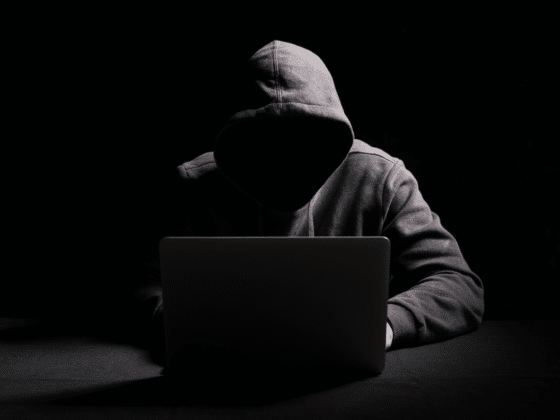 un hacker à capuche sans visage avec un laptop devant un fond noir