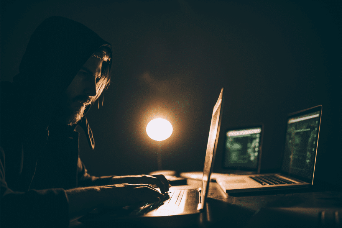 Un criminel devant un laptop dans un espace sombre avec une lampe