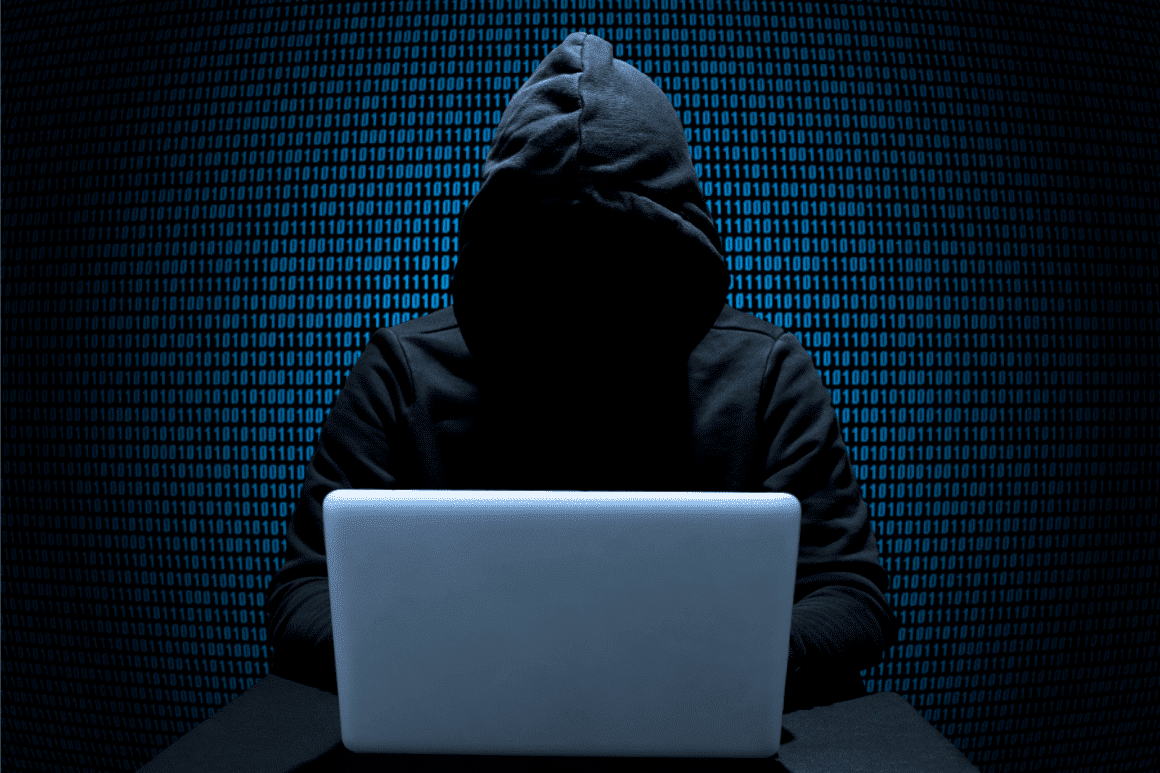 Un pirate à capuche avec un laptop et devant un mur de 0 et de 1