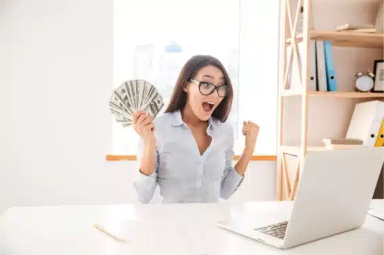 Une femme devant son laptop avec une liasse de billets
