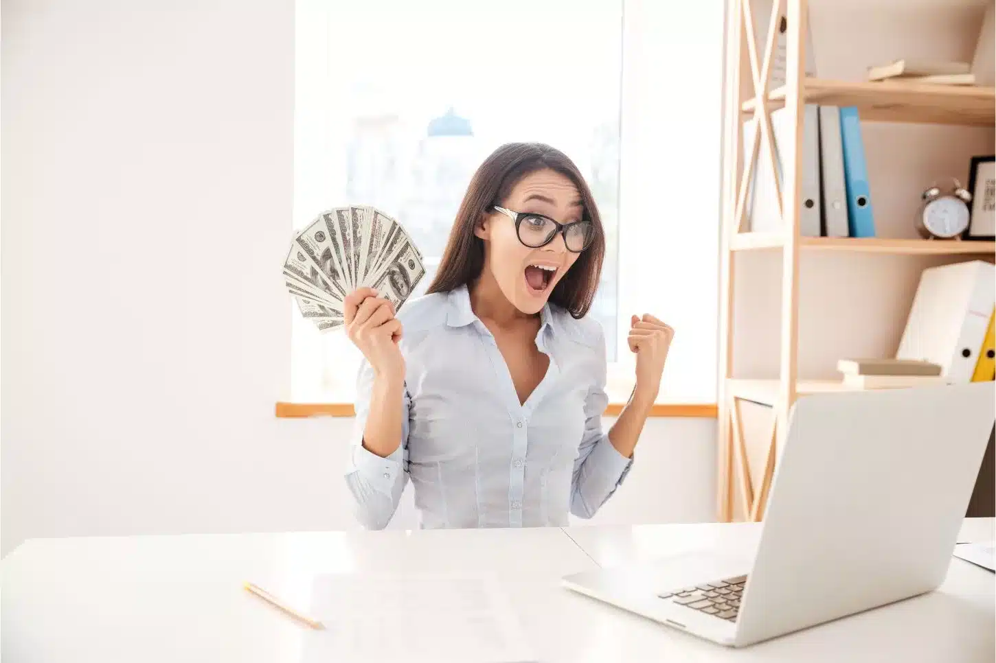 Une femme devant son laptop avec une liasse de billets