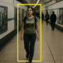 Une jeune femme marche dans un couloir de métro sous vidéosurveillance, encadrée par un rectangle jaune simulant le suivi algorithmique utilisé dans les systèmes de détection comportementale sans reconnaissance faciale.