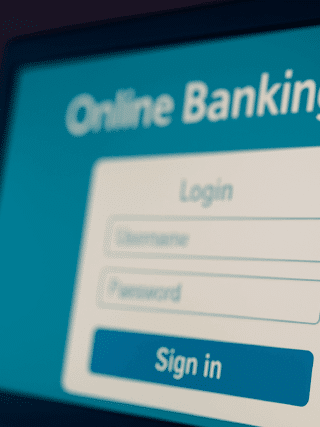 Un hameçon suspendu devant un écran d’ordinateur affichant une page de connexion à une banque en ligne. L’image illustre une tentative de phishing en ligne dans un contexte sobre et moderne, avec un contraste visuel fort pour attirer l’attention sur le risque.
