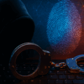 Image symbolique d'une cybercriminalité, montrant une silhouette encapuchonnée derrière un clavier d’ordinateur, des menottes métalliques posées sur les touches, et une empreinte digitale numérique lumineuse en arrière-plan sur fond de réseau digital orange et bleu. L’image évoque le piratage informatique, les arrestations de cybercriminels et l’identification numérique.