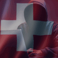 Silhouette encapuchonnée devant un ordinateur portable, symbolisant une cybermenace, sur fond de drapeau suisse translucide et ambiance sombre — évoquant les enjeux de cybersécurité en Suisse