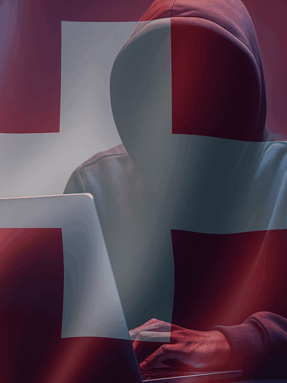 Silhouette encapuchonnée devant un ordinateur portable, symbolisant une cybermenace, sur fond de drapeau suisse translucide et ambiance sombre — évoquant les enjeux de cybersécurité en Suisse