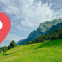 Vue panoramique d’un paysage verdoyant dans les Alpes suisses, avec un pic montagneux en arrière-plan et une icône de géolocalisation rouge au premier plan — illustration d’un test de géolocalisation assistée par intelligence artificielle.
