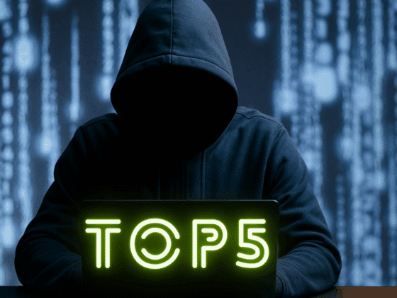 Image réaliste d'une personne encapuchonnée, assise devant un ordinateur portable dans un environnement sombre, illustrant les menaces liées au cybercrime, aux attaques informatiques et à la cybersécurité.
