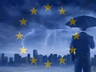 Un homme en costume vu de dos tenant un parapluie, face à une ville sous un orage violent. En surimpression, les étoiles du drapeau européen symbolisent la protection et la coordination de l’Union européenne face aux crises. L’ambiance visuelle évoque la cybersécurité et la résilience en contexte de menace.