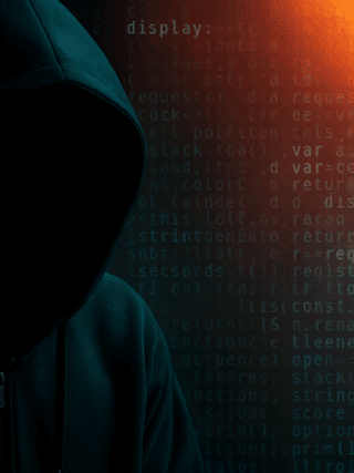 Silhouette sombre d’un individu portant une capuche, symbolisant un hacker, sur fond de code informatique et de lumières rouges et bleues, représentant une cyberattaque ou une activité de piratage.