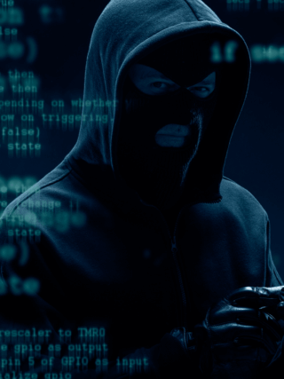 Homme masqué en hoodie, représentant un hacker, utilisant un smartphone dans un environnement numérique avec du code informatique en arrière-plan et une paire de menottes illustrée, symbolisant une arrestation.