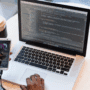 Vue rapprochée d’un développeur travaillant sur une application Android avec un ordinateur portable affichant du code Java dans Android Studio, tout en testant l’application sur un smartphone connecté via USB. Une tasse de café, une paire de lunettes et le logo Android sont visibles sur la table.