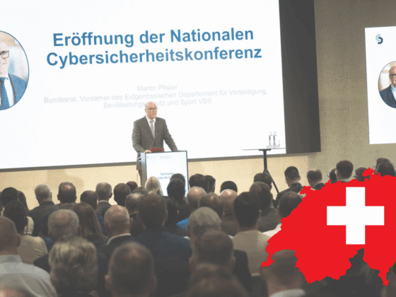 Martin Pfister, conseiller fédéral suisse, prononce le discours d’ouverture de la Conférence Nationale sur la Cybersécurité devant un public attentif, avec une carte rouge de la Suisse ornée d'une croix blanche en premier plan.