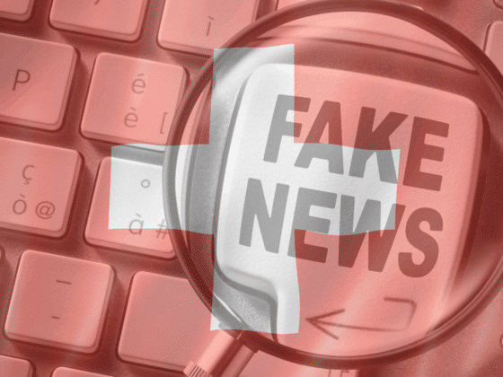 Clavier d’ordinateur avec une touche marquée « FAKE NEWS » vue à travers une loupe, surmontée d’un drapeau suisse en transparence, illustrant la problématique de la désinformation en ligne en Suisse.