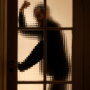 Silhouette floue d'une personne levant le bras de manière menaçante derrière une porte vitrée à petits carreaux, évoquant une scène de tension ou de danger.