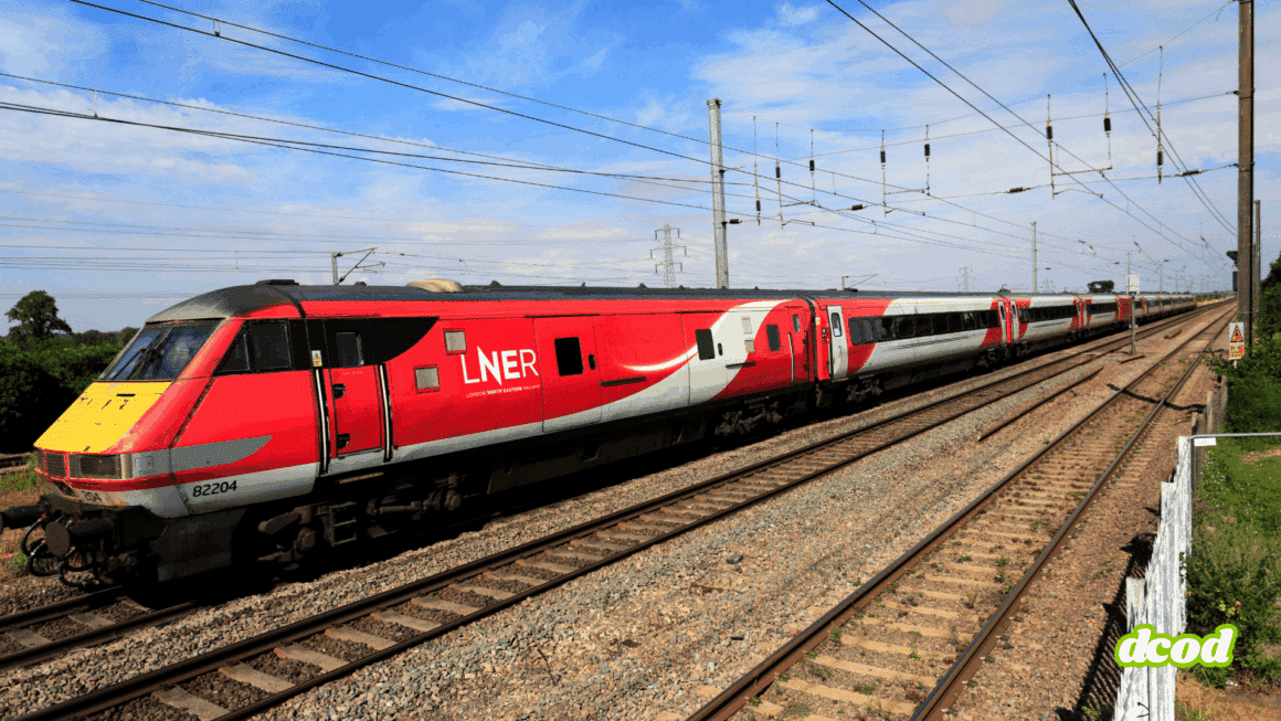 Train à grande vitesse rouge et gris de la compagnie LNER (London North Eastern Railway) circulant sur une voie ferrée électrifiée par une journée ensoleillée, au milieu d’un paysage rural britannique.
