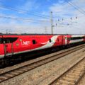 Train à grande vitesse rouge et gris de la compagnie LNER (London North Eastern Railway) circulant sur une voie ferrée électrifiée par une journée ensoleillée, au milieu d’un paysage rural britannique.