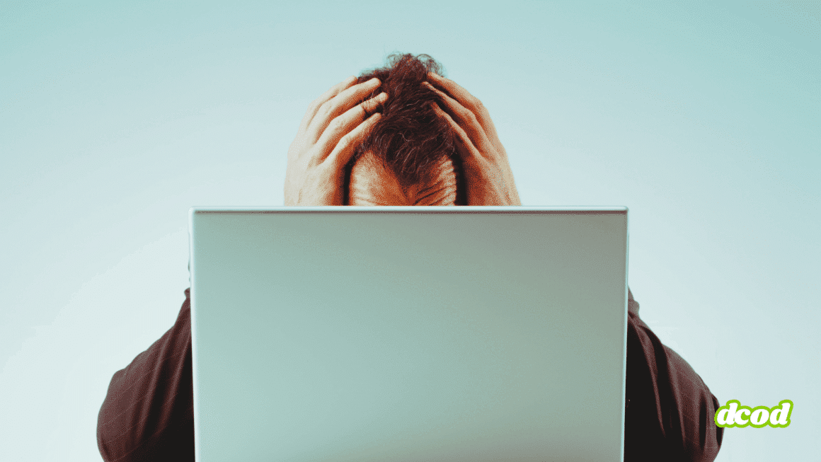 Homme assis, tenant sa tête entre les mains derrière un ordinateur portable, exprimant la détresse ou la surcharge mentale