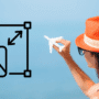 Femme de dos portant un chapeau orange, tenant un avion miniature face à la mer, avec une icône de redimensionnement d’image superposée à gauche et le logo « dcod » en bas à droite.