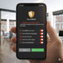 Main tenant un smartphone affichant une fausse alerte système critique de l’application fictive "SecureBank", demandant des autorisations sensibles comme l’accès aux messages, contacts et services d’accessibilité, dans un bureau moderne. Risque de phishing ou de malware.