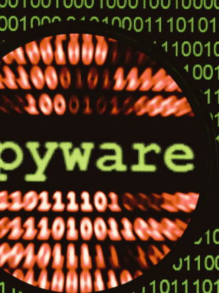 Illustration d’un écran rempli de code binaire vert avec le mot « spyware » mis en évidence par une loupe, représentant la détection de logiciels espions dans un environnement numérique.
