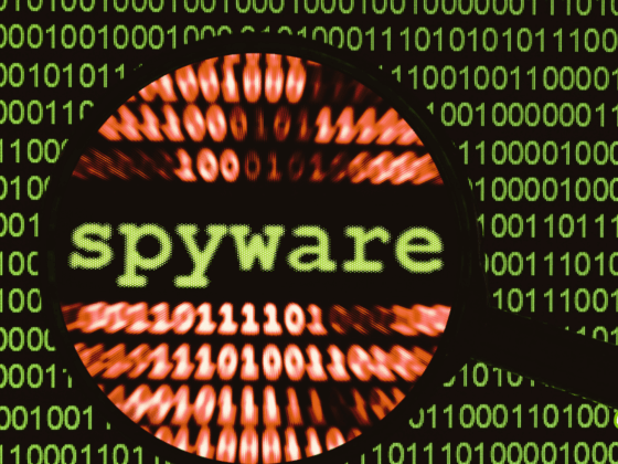 Illustration d’un écran rempli de code binaire vert avec le mot « spyware » mis en évidence par une loupe, représentant la détection de logiciels espions dans un environnement numérique.