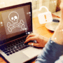 Une personne devant un ordinateur portable dont l’écran affiche une icône de tête de mort symbolisant un malware ou une cyberattaque, avec des pictogrammes d’alerte en surimpression, illustrant un problème de sécurité informatique.