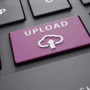 Vue rapprochée d’un clavier d’ordinateur avec une touche violette portant l’inscription « Upload » et une icône de cloud, symbolisant le téléversement de fichiers vers le cloud ou un serveur en ligne.
