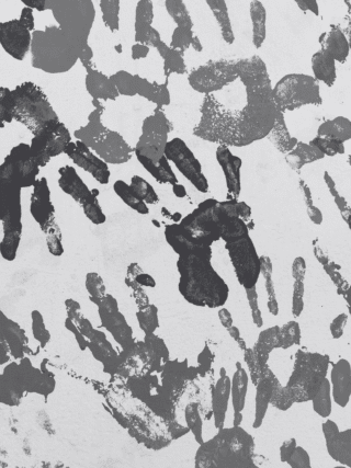 Mur recouvert de multiples empreintes de mains d'enfants peintes en différentes nuances de gris, créant un motif artistique abstrait. Logo « dcod » visible en bas à droite.