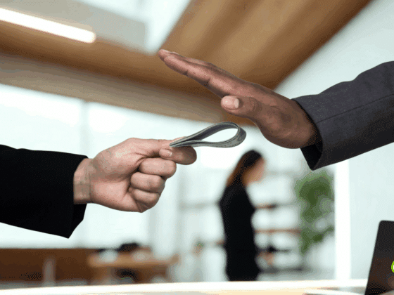 Des hackers tentent de corrompre un journaliste BBC pour infiltrer le réseau 12 Main d’un homme en costume refusant une liasse de billets tendue par une autre personne, symbolisant le rejet de la corruption en entreprise. Scène dans un bureau moderne, avec le logo "dcod" en bas à droite.