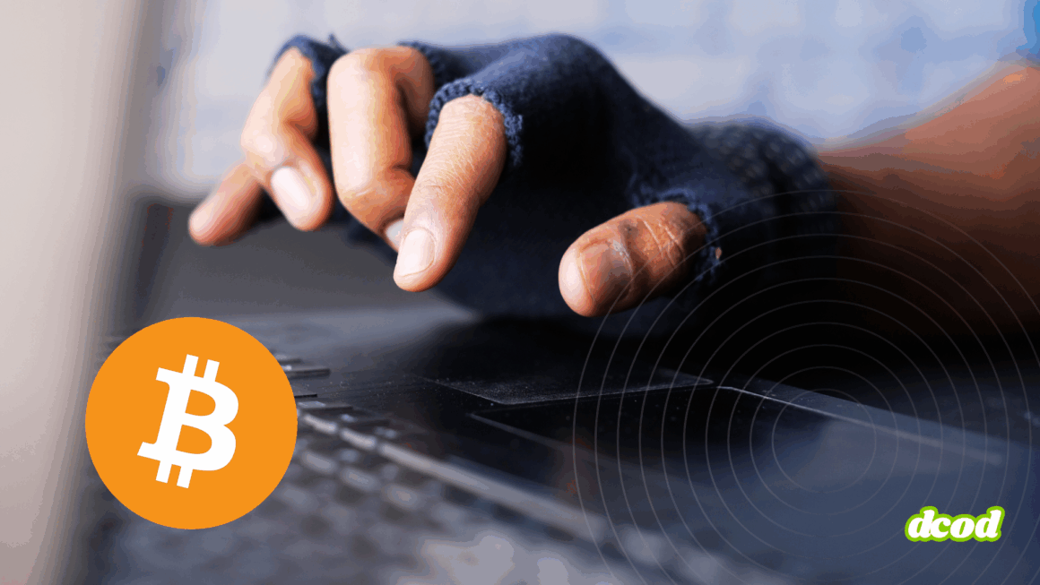 Gros plan sur une main portant un gant sans doigts tapant sur un clavier d’ordinateur, symbolisant une activité potentiellement illégale ou anonyme liée au Bitcoin, représenté par son logo orange en bas à gauche. Logo « dcod » en bas à droite.