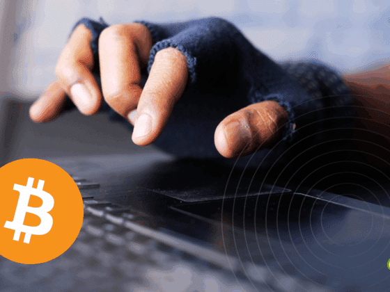 Gros plan sur une main portant un gant sans doigts tapant sur un clavier d’ordinateur, symbolisant une activité potentiellement illégale ou anonyme liée au Bitcoin, représenté par son logo orange en bas à gauche. Logo « dcod » en bas à droite.