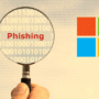 Illustration d’une loupe tenue par une main, mettant en évidence le mot "Phishing" sur un fond de code binaire. À droite, le logo coloré de Microsoft suggère que l’image concerne une tentative de phishing visant les services Microsoft.