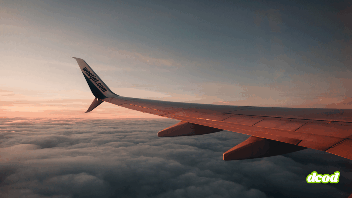Photographie prise depuis le hublot d’un avion WestJet en vol, montrant une aile d’avion survolant une mer de nuages au coucher du soleil, avec le logo "dcod" en bas à droite.