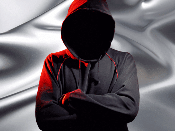 ShinyHunters exploite Salesforce : 39 entreprises victimes de fuites massives 14 Personne non identifiable portant un sweat à capuche noir et rouge, bras croisés, avec le visage dissimulé dans l’ombre, posant devant un fond métallique fluide, symbolisant l’anonymat et la menace cyber dans un univers numérique.