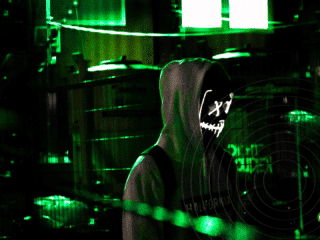 Personne portant un sweat à capuche et un masque lumineux stylisé de type "hacker", se tenant dans un environnement urbain sombre éclairé par des néons verts, avec des grilles métalliques en arrière-plan et le logo « dcod » en bas à droite de l’image.
