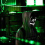 Personne portant un sweat à capuche et un masque lumineux stylisé de type "hacker", se tenant dans un environnement urbain sombre éclairé par des néons verts, avec des grilles métalliques en arrière-plan et le logo « dcod » en bas à droite de l’image.