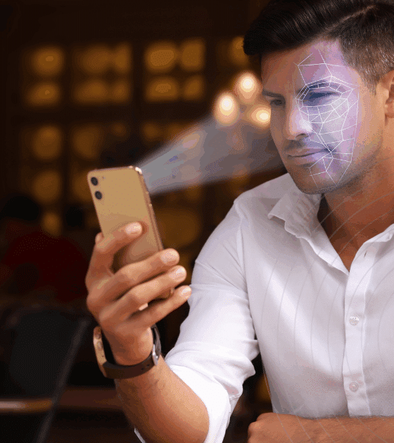 Tinder impose la vérification faciale pour lutter contre les faux profils et les arnaques 36 Un homme utilise la reconnaissance faciale sur son smartphone pour se connecter à une application de rencontre, avec le logo de Tinder visible à gauche de l’image. Un motif numérique est superposé sur son visage pour illustrer le processus de vérification biométrique.