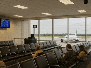 Des hackers piratent les systèmes audio de quatre aéroports en Amérique du Nord 7 Voyageurs assis dans un hall d’aéroport face à un avion sur le tarmac