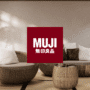 Salon au style japonais épuré avec fauteuils ronds en rotin, lampadaire en bois, tatami au sol et logo MUJI au centre, illustrant l’esthétique minimaliste et naturelle de la marque.