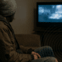 Personne en habits usés assise sur un canapé regardant la télévision