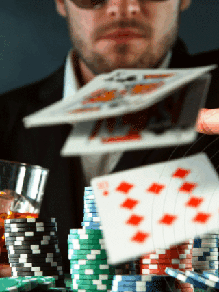 Homme en costume jetant ses cartes lors d'une partie de poker, avec des piles de jetons colorés et un verre de whisky à la main, illustrant l’intensité et le suspense du jeu.